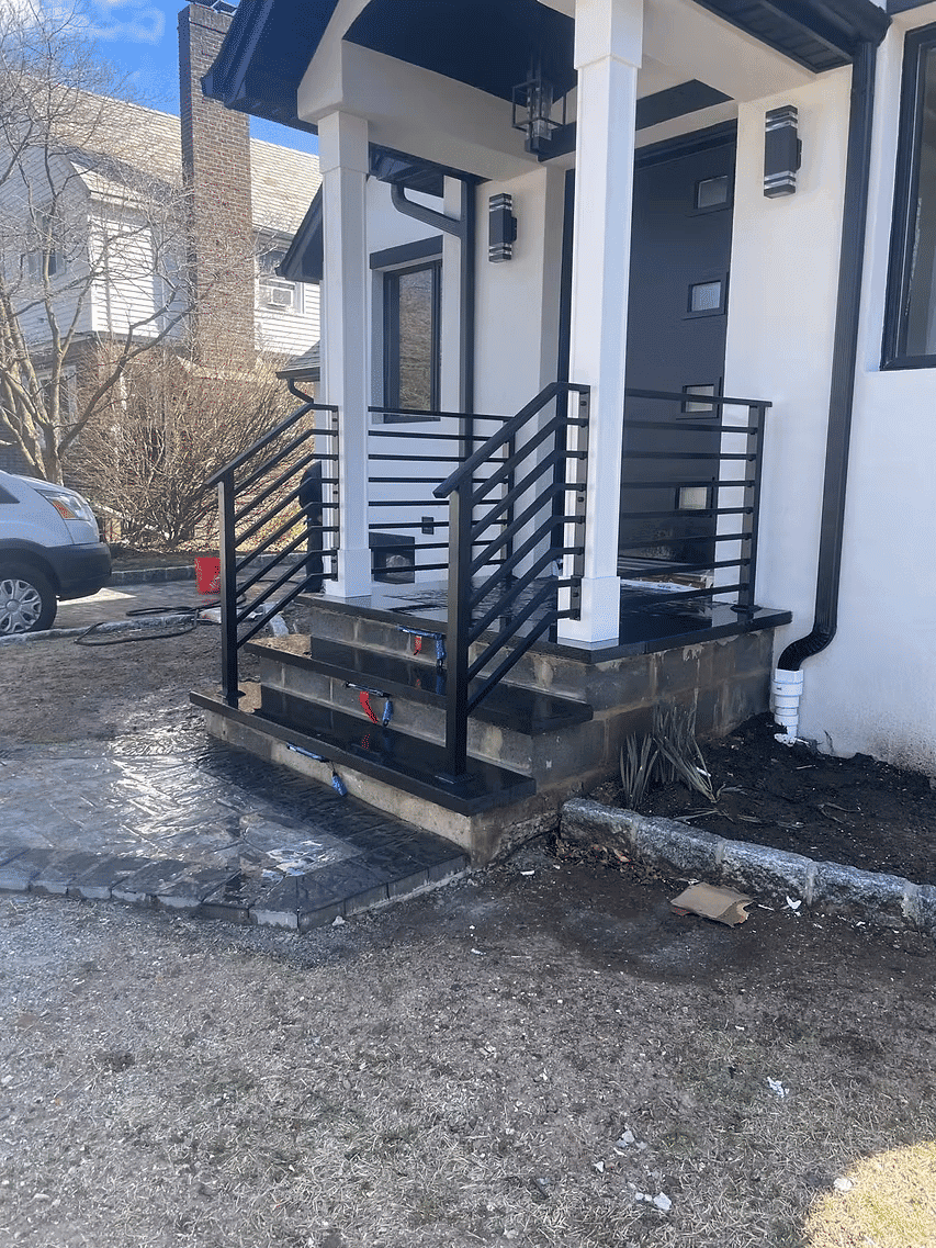 Modern porch with black railing and stone steps leading to a stylish front door.