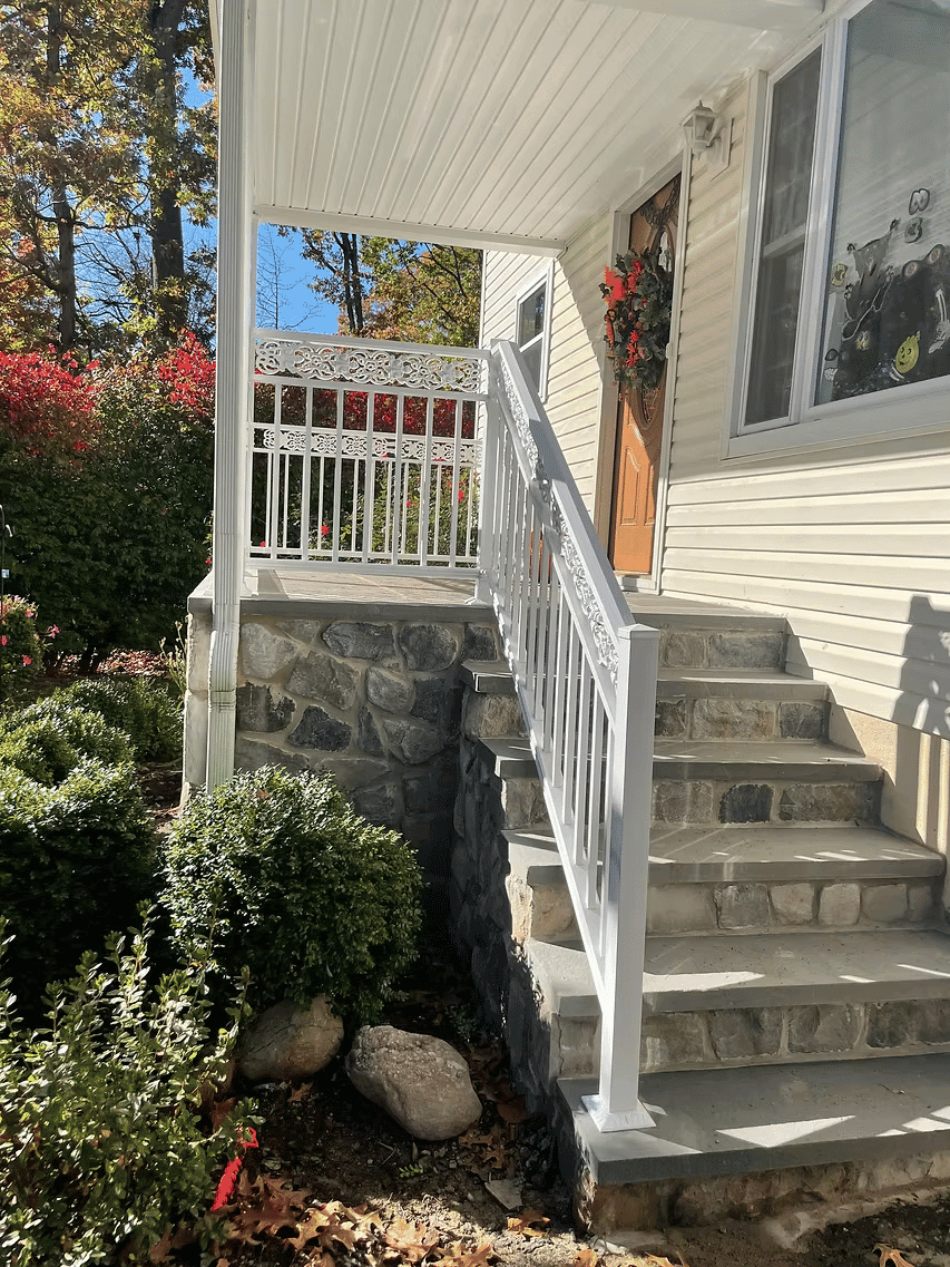 White railing on stone steps leading to a house entrance with autumn foliage.