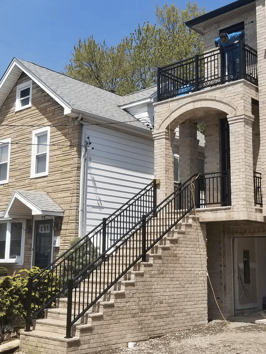 Brick house with balcony, stairway, and worker on upper level in clear blue sky.