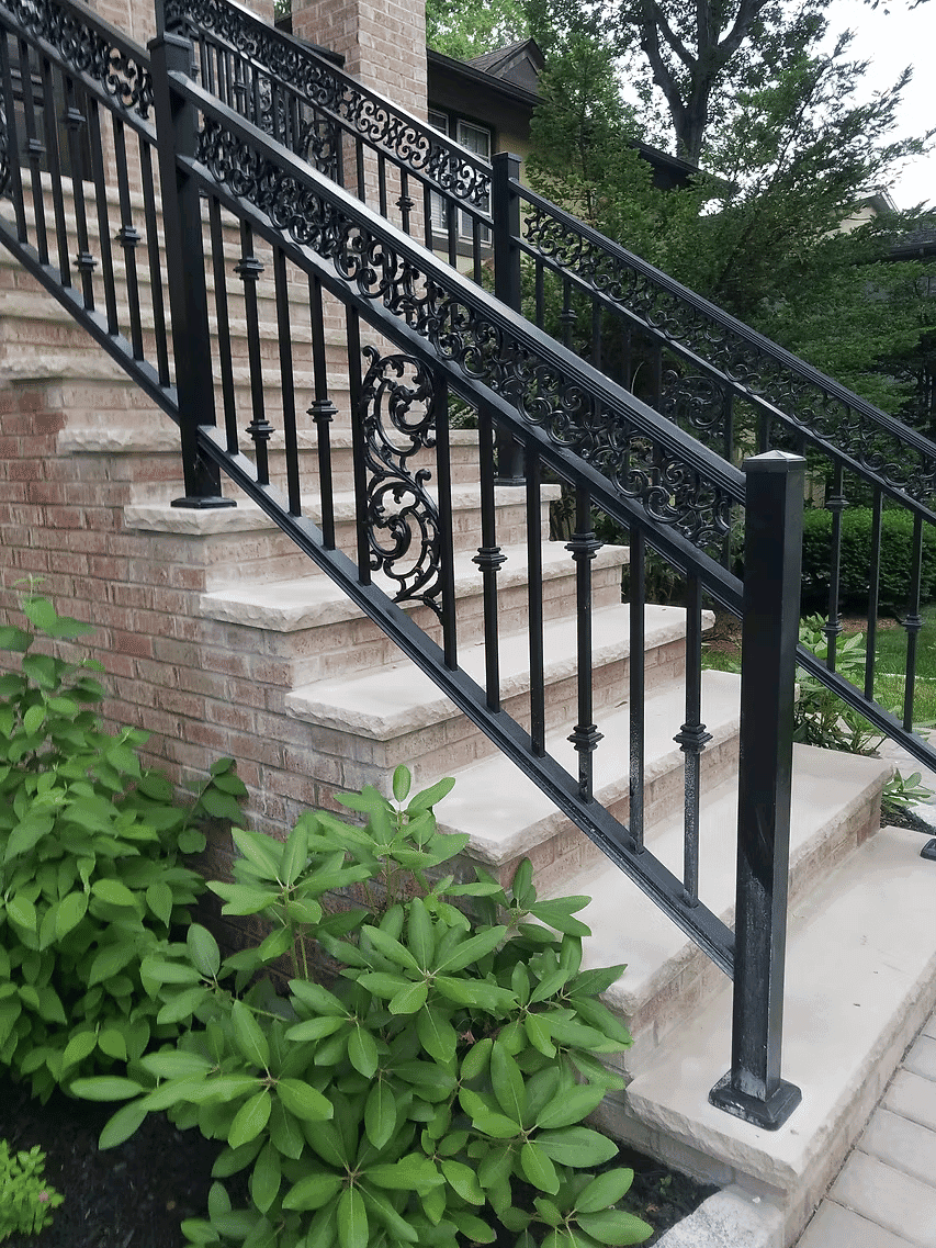 Elegant black wrought iron railing on brick steps with lush green landscaping.