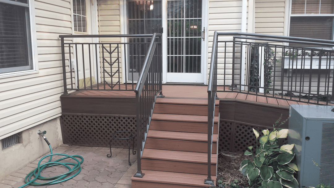 Accessible wooden deck with railing and steps leading to a doorway, featuring plants and utilities.