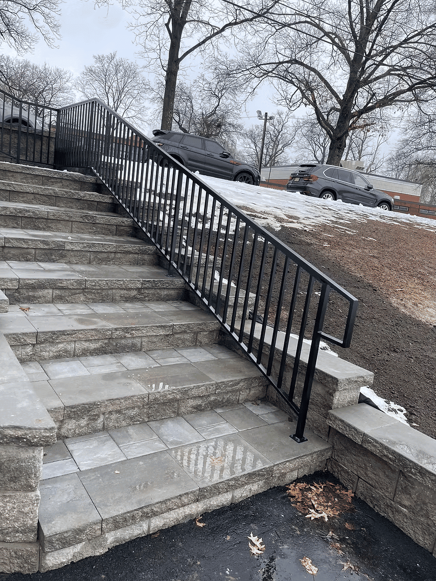 Inclined metal railing beside stone steps with snow, enhancing accessibility for users.