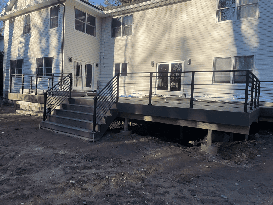 Newly constructed outdoor deck with railings and stairs, attached to a modern home exterior.