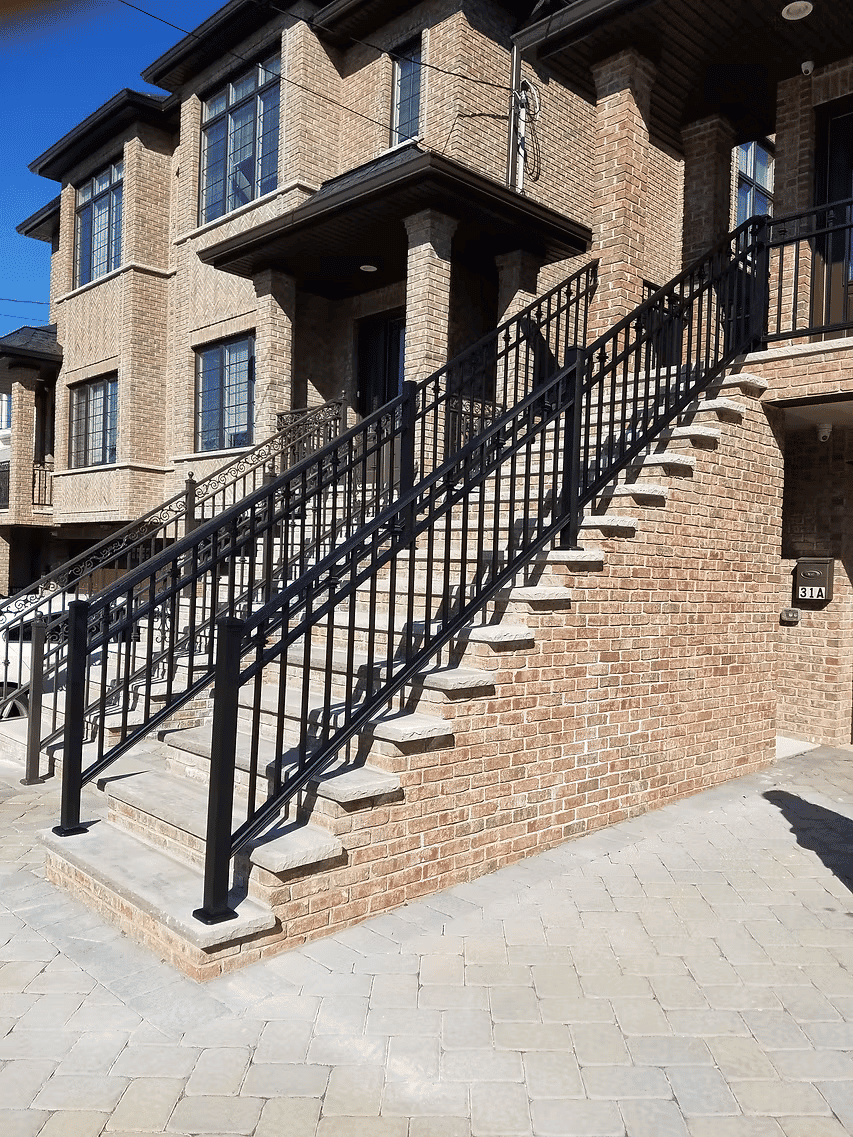 Exterior staircase with black railing leading to brick townhouse entrance.