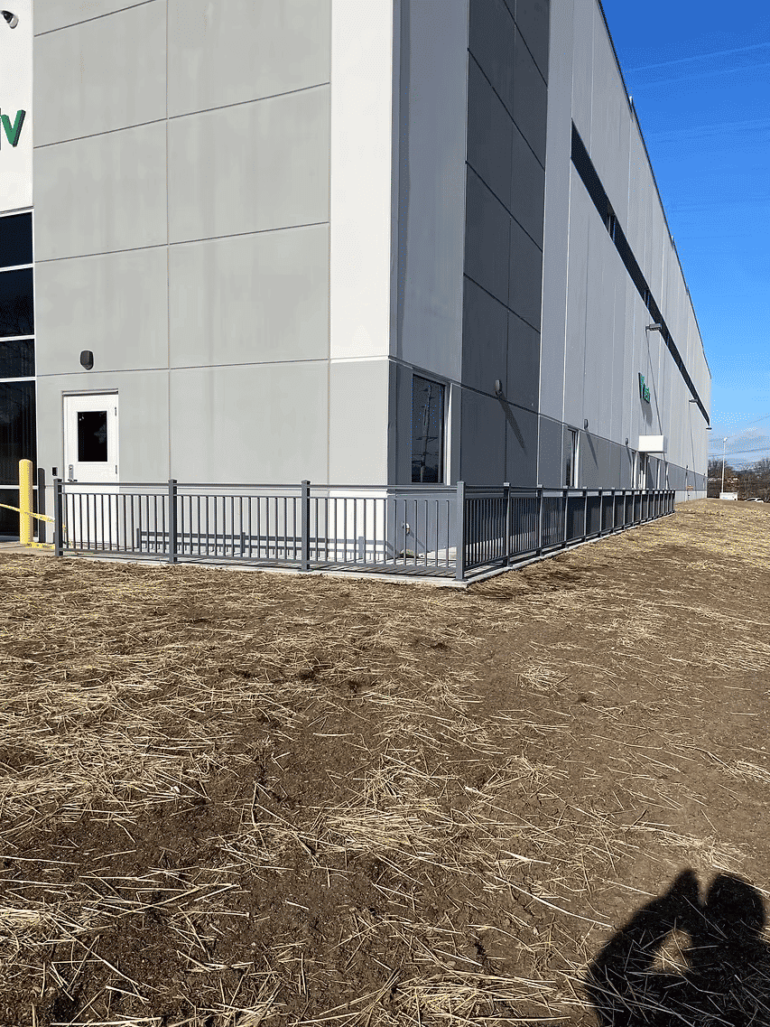 Modern commercial building exterior with gray siding and fenced area, clear blue sky backdrop.