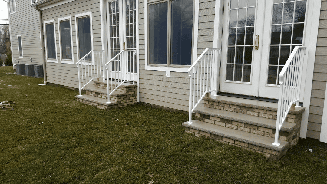 White railings on stone steps leading to a door of a modern home with green lawn.