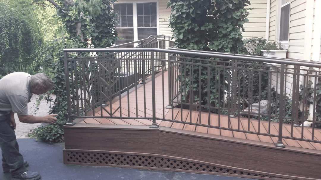Man installing metal railings on a wooden ramp surrounded by greenery at a residential home.