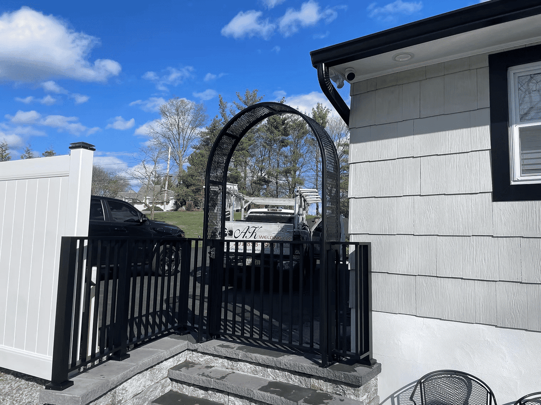 Black archway gate leading to a driveway with a service truck under a clear blue sky.