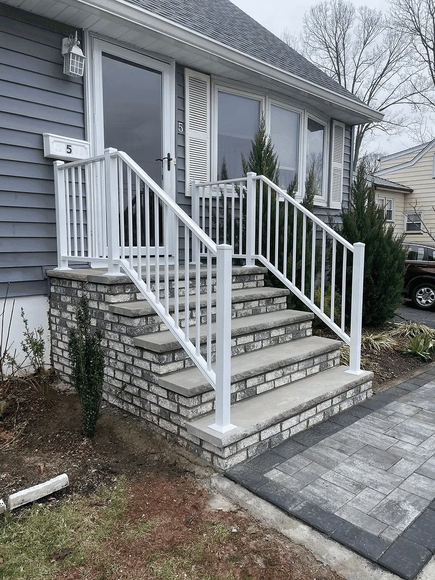 White railing on stone stairway leading to home entrance with landscaping.