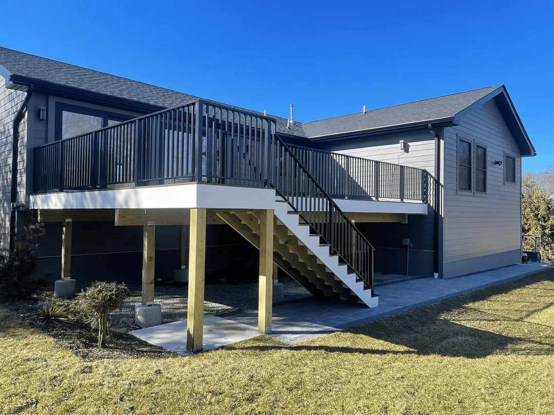 Modern home exterior with a spacious deck and staircase on a sunny day.