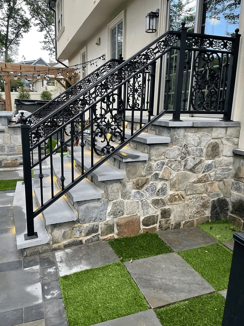 Elegant black wrought iron railing on stone stairs with LED lighting, surrounded by greenery.