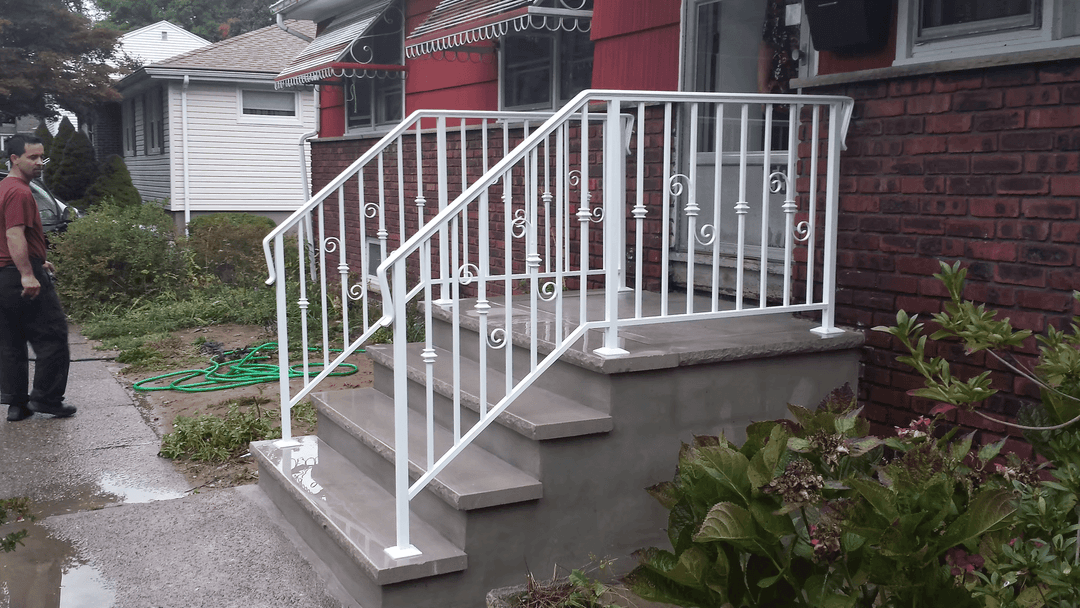 White wrought iron railing on concrete steps outside a red house, with a person standing nearby.