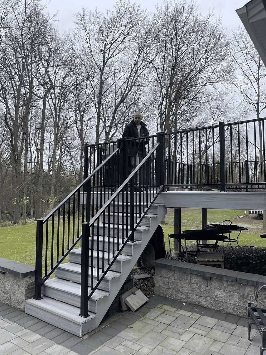 Man standing on a black metal railing staircase in a backyard surrounded by trees.