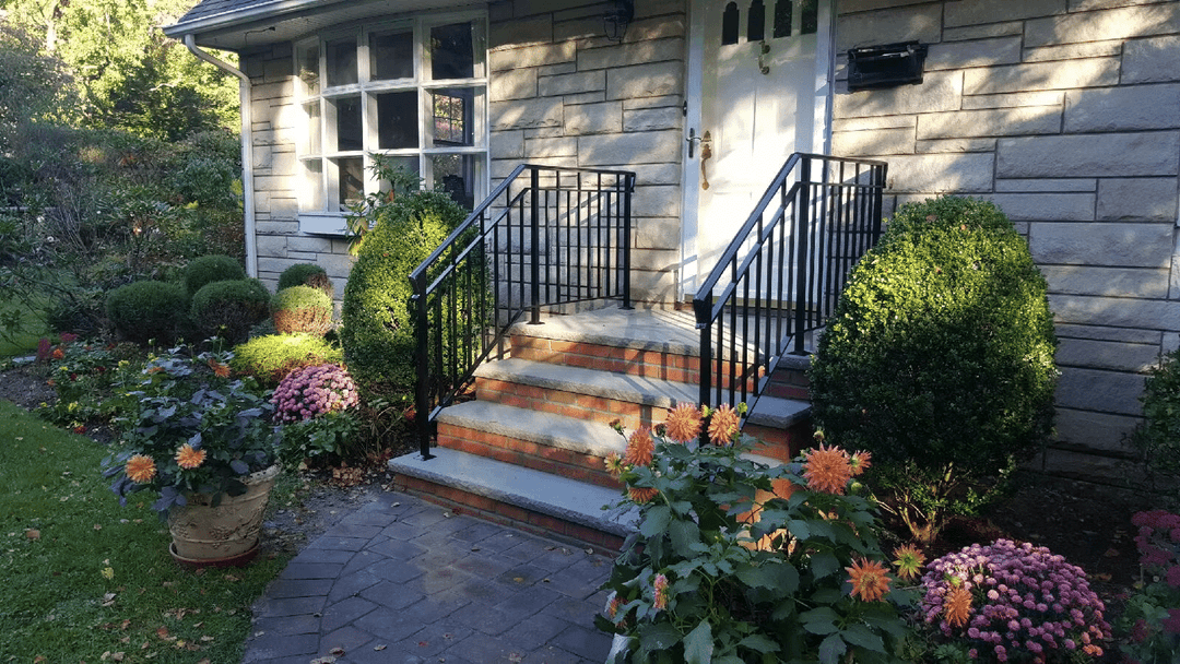 Charming home's entrance with stairs, wrought iron railings, and colorful flower gardens.