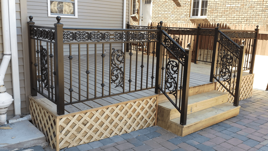 Decorative metal railing on wooden deck steps with lattice skirting in residential backyard.