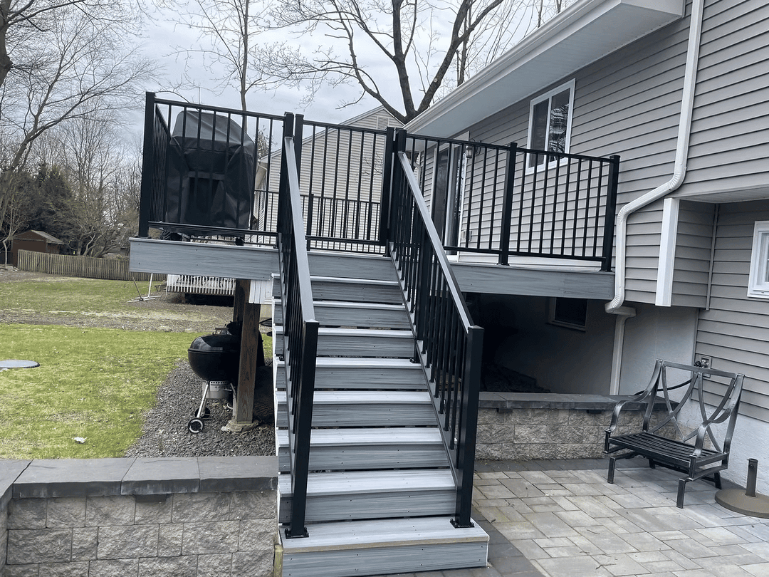 Modern outdoor stairway with black railings leading to a gray house, surrounded by landscaping.