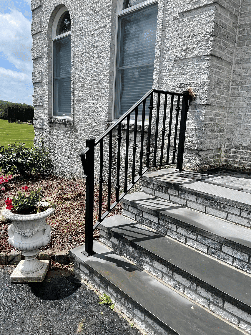 Black metal railing beside stone steps leading to a gray building with flower pot.