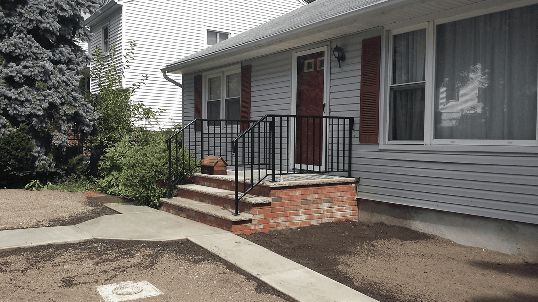 Front entrance of a house with brick steps, metal railing, and landscaped yard.