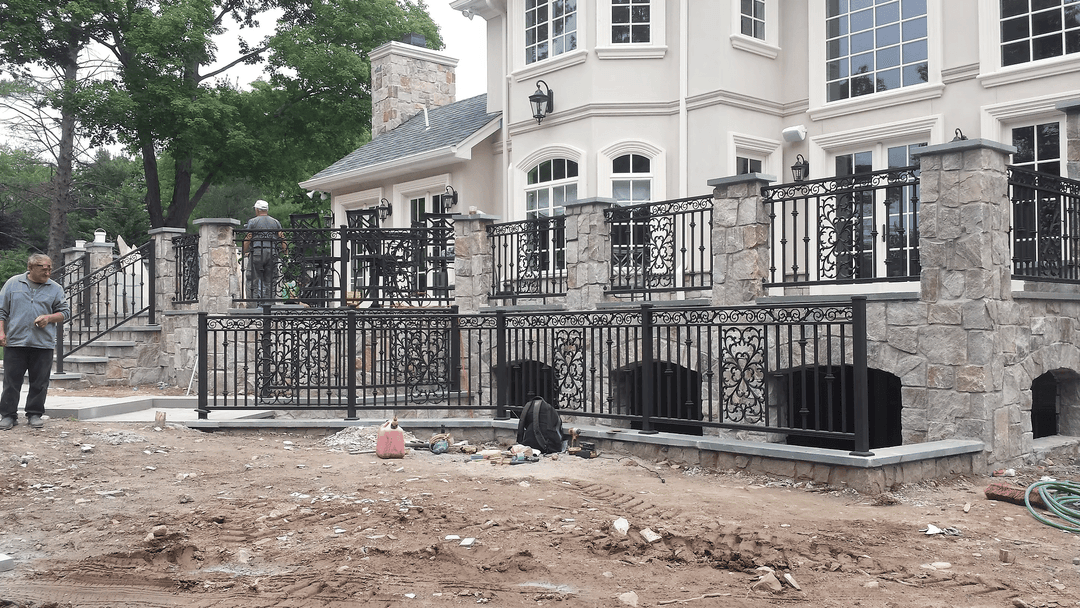 Newly installed black wrought iron railing on a stone wall in front of a large modern home.
