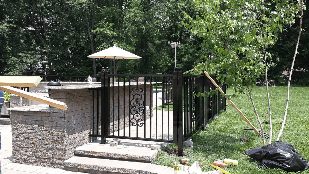 Black metal fence surrounding a pool area with steps, patio, and landscaping.