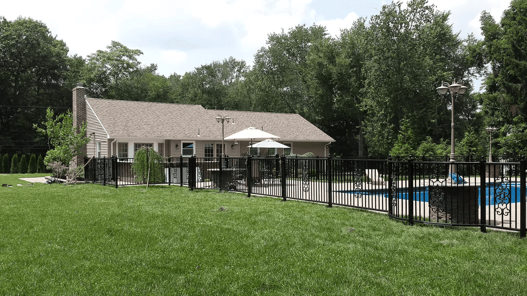 Backyard pool with a fenced patio and house, surrounded by lush greenery and trees.